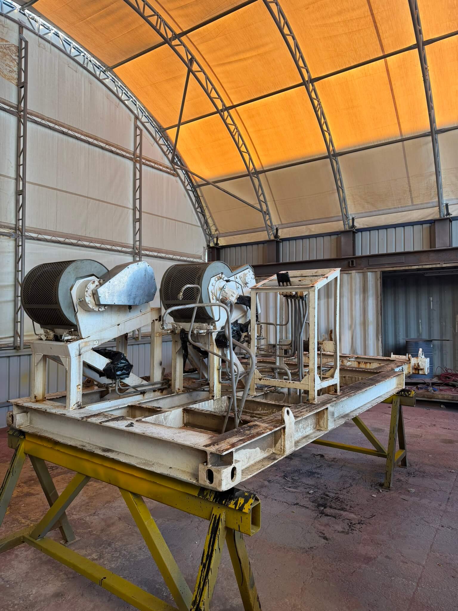 Machinery skid with peeling cream coating, oil residue and rust across the base frame before blasting