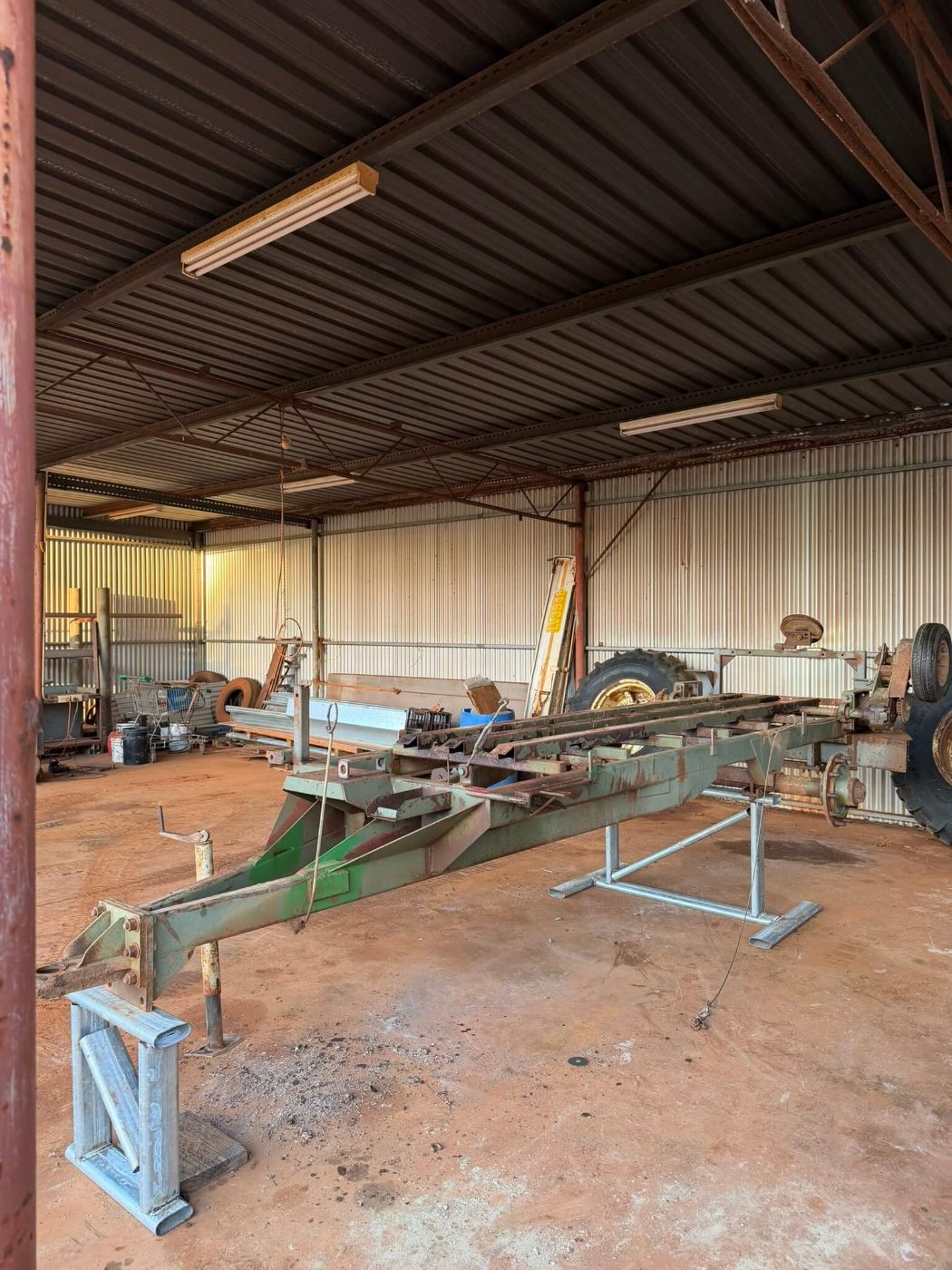 Green seeder bar and frame with rust through the paint, sitting on stands in a farm shed before blasting