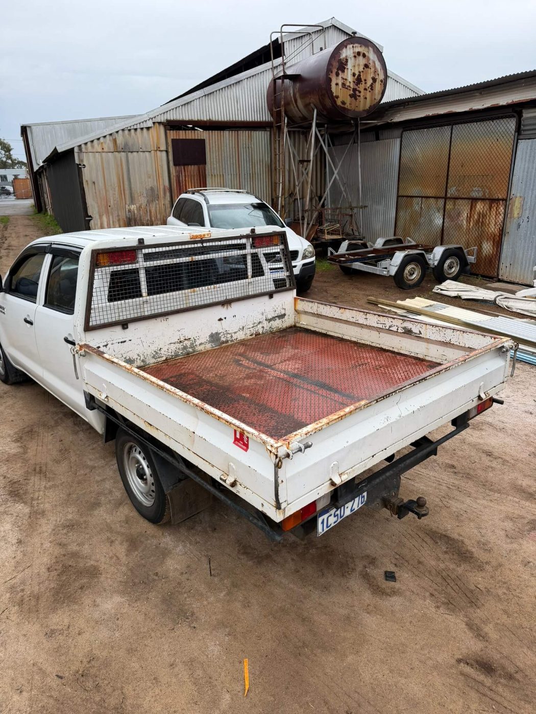 Dual-cab ute tray with rust along the drop sides and a corroded red checker-plate floor before soda blasting