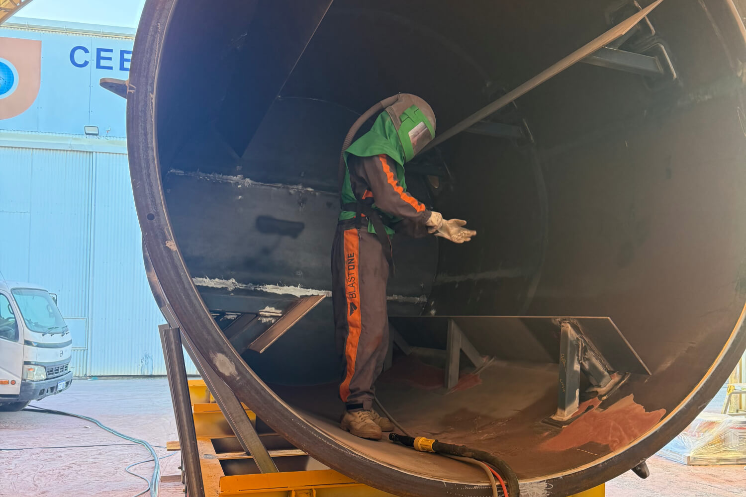 Operator in blast overalls preparing the inside of a large steel tank in the workshop