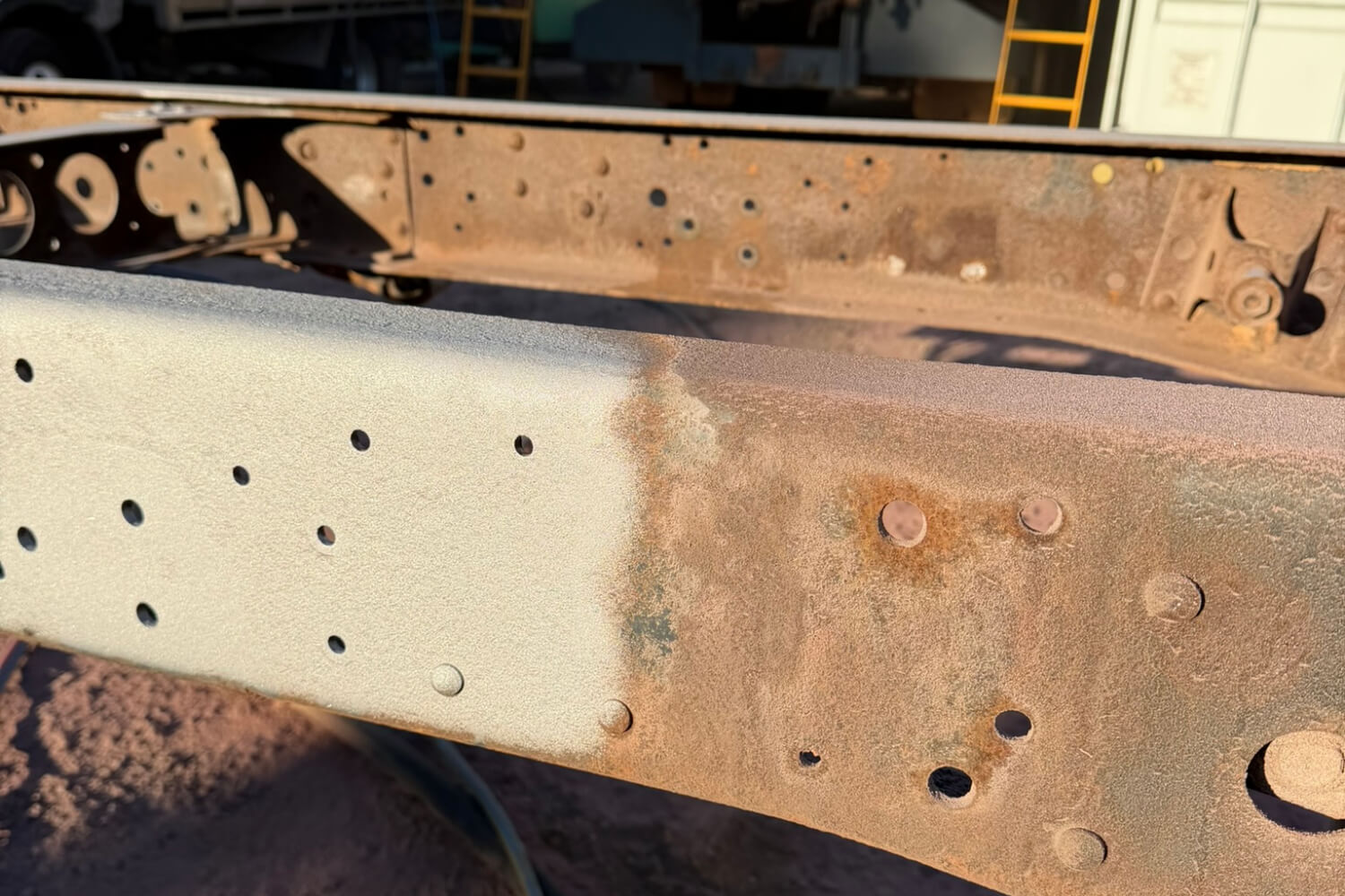 Truck chassis rail half blasted back to bare steel, showing rust and old coating alongside the clean finish