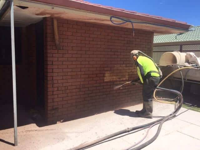 Yellow brick house wall half stripped of paint in Perth