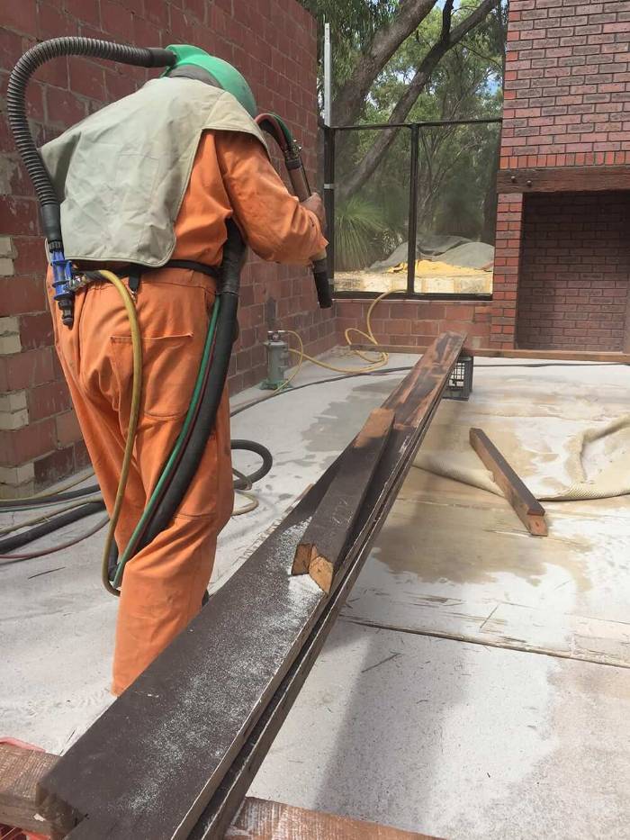 Blaster stripping a hardwood beam on site without gouging the grain